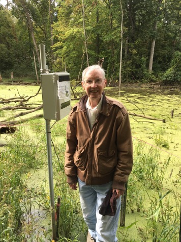 Elderly man posing in a shallow river with equipment